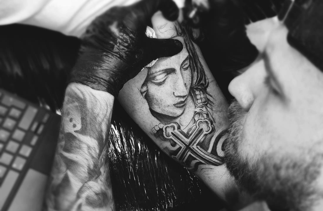 profesjonalny tatuator wykonuje tatuaż na ręce na kursie tatuażu. Tatuaż przedstawia kobietę i krzyż
